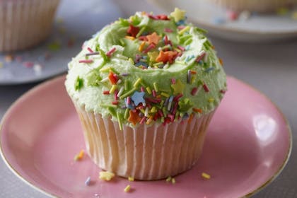A vanilla cupcake with green frosting and sprinkles