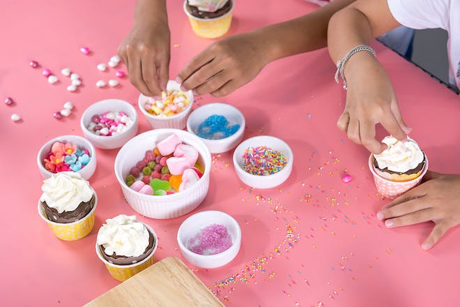 kids decorating cupcakes with bowls full of sweets and sprinkles