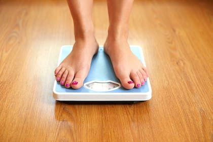 woman's feet standing on blue weighing scales on wooden floor